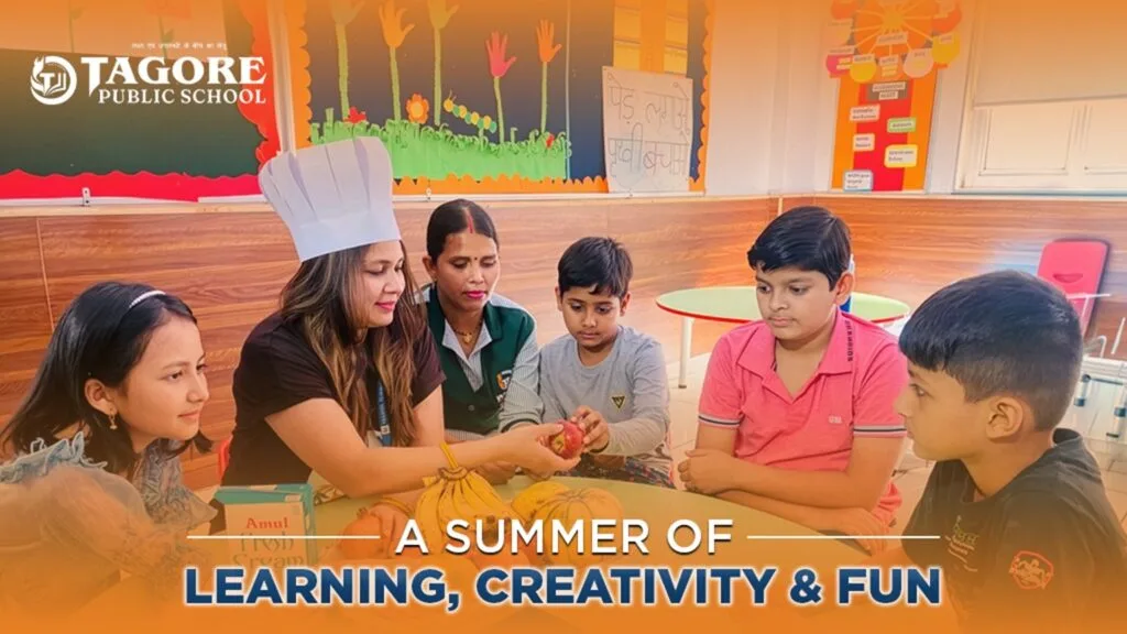 A female teacher wearing a white chef's hat holds up a red apple to show a group of five students sitting around a table. The table has various fruits and a box of fresh cream. Text on the image reads "Tagore Public School - A Summer of Learning, Creativity & Fun."